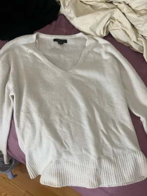 Vit v-ringad stickad tröja Amisu - Säljer en vit stickad tröja från Amisu med v-ringad hals och långa ärmar. Tröjan har bred ribbad kant nedtill och är mjuk i materialet, perfekt för att hålla sig varm under kyliga dagar. Enkel och stilren design som funkar till många outfits.