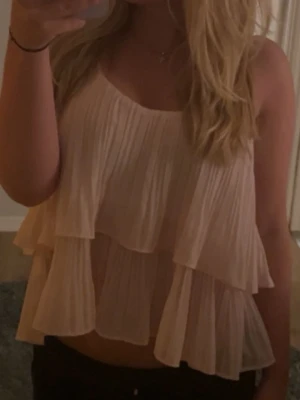 Ljusrosa volang linnetopp - Säljer en ljusrosa linnetopp med dubbla lager volanger och plisserad struktur. Toppen är ärmlös och har en luftig, loose passform som ger en skön och avslappnad vibe. Perfekt för varma dagar och sommarhäng.