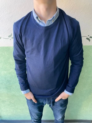 Marinblå merinotröja från Riley - Säljer en stilren marinblå tröja från Riley i fin merinoull. Tröjan har rund halsringning och långa ärmar, perfekt för lager på lager. Enkel och klassisk design som funkar till skjorta eller t-shirt under.