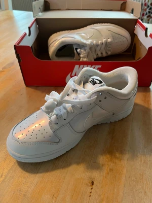 Nike Dunk Low SE Just Do It White Iridiscent Helvita Women’s - Helt nya och oanvända Nike Dunk Low sneakers i helvit färg med klassisk design. Skorna har snörning, rund tå och platt sula. Iriserande färg på delar av skon. Med snygga ”Just Do It” detaljer på skorna. Skriv för mer bilder 😊🌷