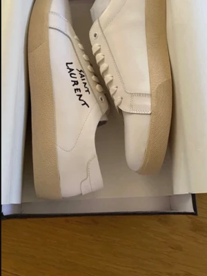 Saint Laurent skor vita 41  - Säljer ett par stilrena vita sneakers från Saint Lauren i storlek 41 endast testade inomhus men som tyvärr inte passad⭐️ Obs ingen dustbag medföljer, bara att höra av sig vid frågor jag svarar så snabbt som möjligt / Vincent ⭐️