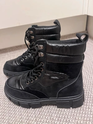 Chunkey boots med snörning - Svarta chucken boots med grov sula och snörning. Ovandelen är i en kombination av skinn och syntet material, som ger en snygg look. Storlek 37. Mycket bra skick! 