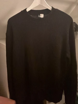 Svart stickad tröja från H&M - En enkel svart stickad tröja från H&M i storlek S. Tröjan har rund hals och långa ärmar med ribbade muddar vid halsen, ärmslut och nederkant. Perfekt för lager-på-lager och chill dagar.