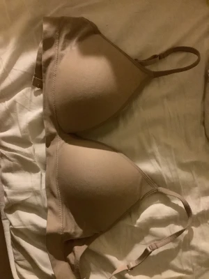 Beige bh med smala axelband - Säljer en enkel och stilren beige bh med smala justerbara axelband. Toppen har en mjuk och slät yta, perfekt att bära under andra plagg. Färgen är neutral och passar till det mesta.