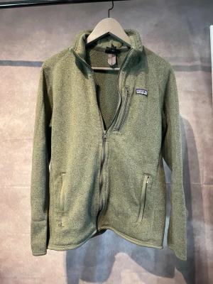 Patagonia Fleece - Säljer en grön fleecejacka från Patagonia i storlek M. Jackan har hel dragkedja framtill, två sidofickor med dragkedja och en liten logga på bröstet. Perfekt för kyliga dagar och outdoor-aktiviteter. Mjuk och skön fleece som håller värmen. Sitter lite mindre 