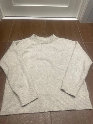 Beige stickad tröja - Mysig beige stickad tröja med rund halsringning och ribbade muddar vid ärmslut och nederkant. Perfekt för kyliga dagar och enkel att matcha med olika outfits. Klassisk och stilren design som passar till det mesta.