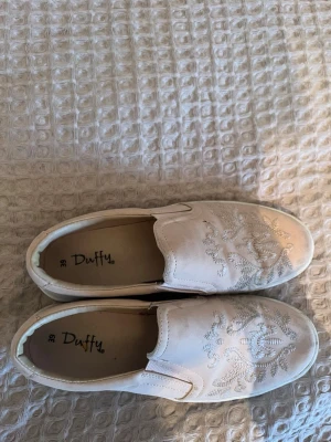 Ljusrosa slip-on sneakers från Duffy - Säljer ett par ljusrosa slip-on sneakers från Duffy i storlek 39. Skorna har broderade detaljer på ovandelen och en vit sula. De är har en platt sula med rund tå. Perfekta för dig som gillar stilrena skor, men med något extra.