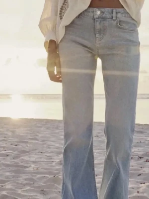 Bootcut ljusblå jeans - Säljer ett par ljusblå bootcut jeans med klassisk femficksdesign och knappgylf. Jeansen har en högre midja och är tillverkade i mjukt denimtyg som ger en skön passform. Perfekta för dig som gillar retrovibbar och vill ha en snygg siluett. Storlek 38 men passar mig som har 36. 