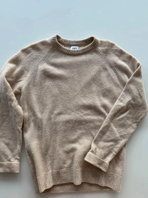 Beige stickad tröja från Zara - Säljer en beige stickad tröja från Zara i storlek M. Tröjan har rund hals, ribbade muddar vid ärmslut och nederkant samt långärmad design. Perfekt för dig som gillar enkel och stilren look med mjukt material.