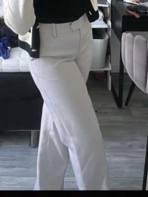 Beiga wide kostymbyxor - Snygga beiga kostymbyxor med wide fit och hög midja. Byxorna har klassiska bälteshällor och raka ben som ger en clean och modern look. Perfekta att styla med sneakers eller loafers för en trendig vibe.