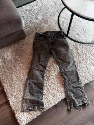 Gråa flared jeans från Zara - Säljer ett par grå jeans från Zara i rak modell med klassisk femficksdesign. Jeansen har normal passform och är tillverkade i bomullsmaterial. Färgen är mörkgrå och benen har råa, slitna kanter för en cool vibe.