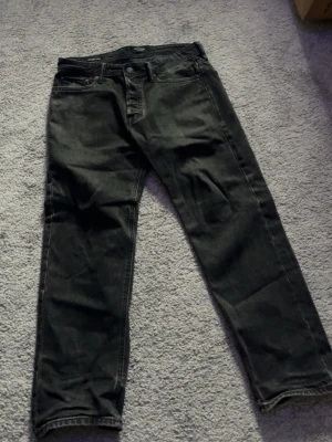 Svarta jeans med straight fit - Säljer ett par svarta jeans med klassisk femficksdesign och rak passform. Jeansen har knapp och dragkedja framtill samt bakfickor. Materialet är robust denim som ger en cool och tidlös look.