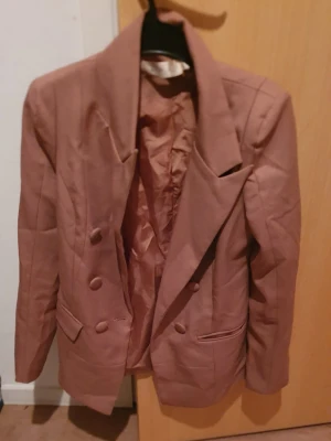 Kavaj - Säljer en brun kavaj med dubbelknäppning och breda slag. Kavajen har två fickor framtill och är helfodrad. Perfekt för dig som vill ha en stilren och klassisk look. Passar lika bra till jeans som till kostymbyxor.