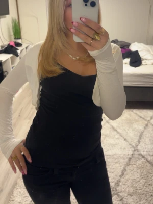 Vit bolerotopp med spetsrygg - Säljer en vit bolerotopp med lång ärm och snygg spetsdetalj över ryggen. Toppen är croppad och har en tight passform som sitter snyggt över axlarna. Perfekt att styla över linnen eller klänningar för en trendig look.