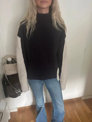 Svart och beige polotröja stickad - Säljer en jättefin stickad polotröja i svart och beige. Tröjan har högt ribbat krage, breda beige ärmar och svart framsida. Passformen är loose och ärmarna är långärmade. 