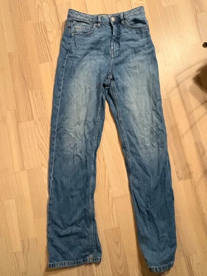 Blå jeans DENIM 1953, rak modell - Snygga blå jeans från DENIM 1953 i rak modell med klassisk femficksdesign. Jeansen har normal passform och är tillverkade i hållbar denim med guldfärgade detaljer på insidan av linningen. Perfekta för dig som gillar enkel och tidlös stil.