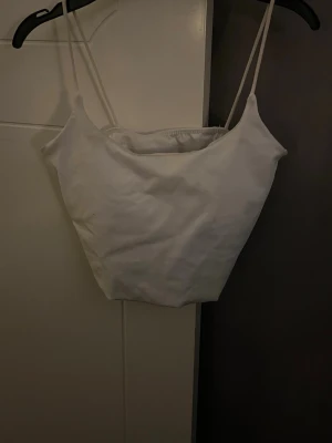 Vit bandeau linnetopp med smala band - Säljer en stilren vit bandeau linnetopp med smala axelband. Toppen har en enkel och clean design, är ärmlös och har en lätt croppad passform. Perfekt att matcha med jeans eller kjol för en fräsch look.