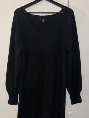 Svart stickad långklänning från Bik Bok - Mysig svart stickad långklänning från Bik Bok med v-ringad hals och långa ärmar. Klänningen har ribbade muddar vid ärmslut och är perfekt för dig som gillar enkel och stilren design. Passar dig som vill ha en bekväm och snygg look.