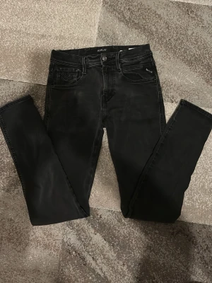 Replay svarta jeans med  slim passform - Svarta jeans från Replay med klassisk femficksdesign och smal passform. Jeansen har svarta sömmar, knappstängning och bälteshällor. Materialet är stretchigt jeans och färgen är mörk svart med lätt tvättad look. Perfekta för dig som gillar stilrena och moderna jeans.