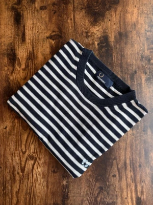 Fred Perry Tröja - Fred Perry tröja i klassisk casuals/old money-stil. Välvårdad och i bra skick utan hål, fläckar eller slitage. Tidlös design med diskret logotyp, stark koppling till brittisk casuals-kultur. Perfekt både till vardag och mer uppklädda outfits. Ett stilrent plagg som aldrig går ur tiden.