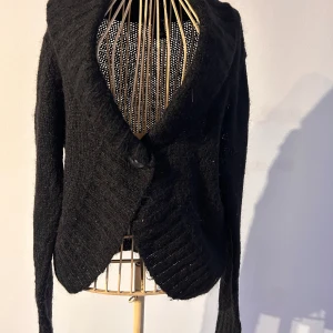 Svart stickad kofta från H&M - Säljer en svart stickad kofta från H&M. Koftan har en mysig och varm design med långa ärmar och en stor krage. Perfekt för kyliga dagar och kan enkelt matchas med olika outfits. 30% mohair vilket gör den mjuk. Stl M. Lite nopprig men kan lätt dras bort.