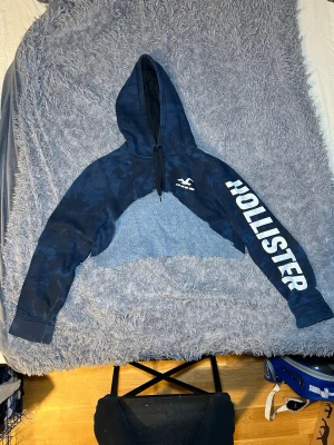 Hollister avklippt Hoodie XL Blå  - Hollister hoodie i storlek XL. Huvtröjan är blå och har tryck med varumärkets namn på ärmen och bröstet. Passar för vardagligt bruk och erbjuder komfort och värme. Jag har klippt den.
