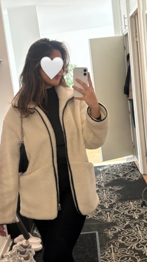 Vit teddyjacka med dragkedja - Säljer en mysig vit lite oversized teddyjacka med hel läder dragkedja framtill och två stora fickor. Jackan har en mjuk och fluffig känsla, perfekt för kyliga dagar. Passformen är normal och ärmarna är långärmade. Enkel och stilren design som är lätt att matcha.