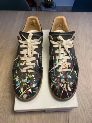Maison Martin Margiela Paint Splatter Low  - Svarta Maison Margiela Paint Splatter skor i mycket bra skick. Skick: 8,5/10. Slitningarna syns i bild 6-7. Storlek 40 men passar 41-41,5. Låda tillkommer. Skorna är äkta! Skicka ett meddelande vid funderingar, bilder osv. 