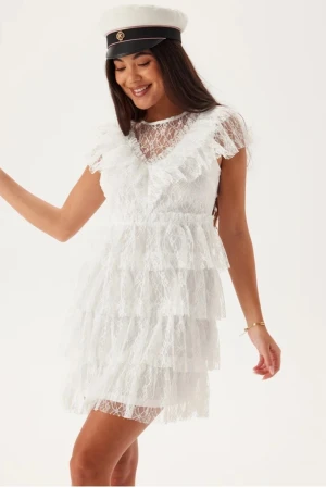 Vit spetsklänning med volanger - Superfin vit kort klänning i spets med flera lager volanger och v-ringning. Klänningen är ärmlös och har en romantisk känsla med sina spetsdetaljer. Perfekt till student eller sommarens festligheter mm. Använd en gång, men har uppsydda ärmar pga göra den mindre kortare i v-ringningen