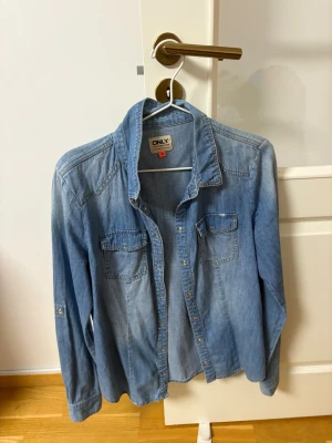 Blå jeansjacka från ONLY, strl 40 - Säljer en klassisk blå jeansjacka från ONLY i storlek 40. Jackan har långa ärmar, två bröstfickor med knappar och snygga sömmar. Perfekt att slänga på över en t-shirt för en chill look. Passar dig som gillar enkel och tidlös stil.