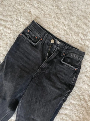 Svarta jeans från ginatricot perfect jeans, strl 32 - Säljer ett par svarta jeans från ginatricot perfect jeans i storlek 32. Jeansen har klassisk femficksdesign, kopparfärgade nitar och dragkedja. Materialet är jeans och färgen är mörk svart med lätt tvättad look. Passar dig som gillar en enkel och stilren vibe. 