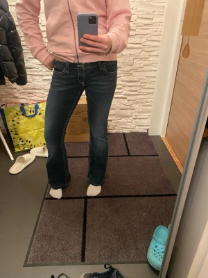 Blå bootcut jeans med broderade fickor - Snygga mörkblå bootcut jeans med kontrastsömmar och broderade detaljer på bakfickorna. Jeansen har låg midja och är tillverkade i klassiskt jeansmaterial. Obs de är uppklippta nere vid benen så att de är längre. 