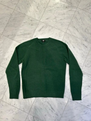 Grön stickad tröja från Uniqlo - Säljer en mörkgrön stickad tröja från Uniqlo med rund hals och ribbade muddar vid ärmslut och nederkant. Tröjan har en enkel och clean design, perfekt för dig som gillar stilrena plagg. Passar dig som vill ha en klassisk look.