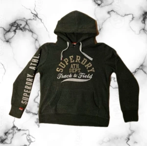 Superdry Hoodie - Svin fet felfri superdry hoodie i storlek S. Den har en klassisk känguruficka därfram och är mörkgrön men kan uppfattas grå i vissa ljussättningar. Priset kan diskuteras.