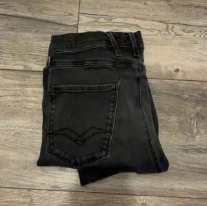 Replay Hyperflex svarta jeans - Svarta Replay Hyperflex Anbass jeans med slim fit och klassisk femficksdesign. Jeansen har stretchigt material för extra komfort och snygga detaljer på bakfickorna. Passar dig som gillar en modern och stilren look med smal siluett. W28/L32