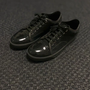 Lanvins - Snygga svarta sneakers från Lanvin med ovandel i mocka och glansig tå i skinn. Klassisk låg modell med snörning och rund tå. Perfekta för dig som gillar stilrena och exklusiva skor med en twist. Diskret Lanvin-logga på sulan. Knappast använda. Storlek 42EU/8UK men passar 43. OBS! Medföljs av låda,skor och ena dustbagen eftersom att jag tappade bort den andra.