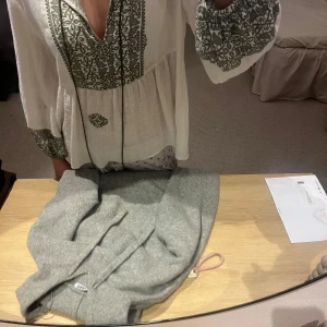 Vit blus med broderi från Zara - Supersöt vit blus från Zara med grönt broderat mönster längs v-ringningen, ärmsluten och nertill. Blusen har långa, vida ärmar och snörning med tofsar framtill💕