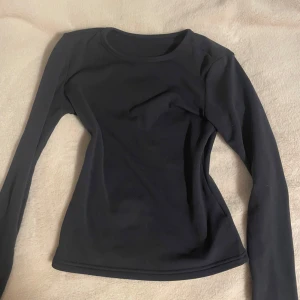 Svart långärmad tröja från Dazy - En marinblå långärmad tröja från Dazy x StarSeries i figurnära modell. Tröjan har rund halsringning och är tillverkad i ett mjukt, stretchigt material som känns skönt mot huden. Perfekt att styla med jeans eller kjol för en clean look.