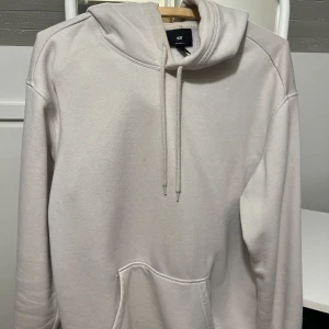 Ljusbeige hoodie från H&M - Säljer en stilren ljusbeige hoodie från H&M med klassisk känguruficka och snörning i huvan. Perfekt för dig som gillar en enkel och clean look. Mjuk bomullsblandning och långärmad modell.