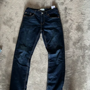 Levi's 511 mörkblå jeans - Säljer ett par mörkblå Levi's 511 jeans med klassisk femficksdesign och snygga kontrastsömmar. Jeansen har normal/slim passform och raka ben, tillverkade i slitstarkt denimtyg. Perfekta för dig som gillar en tidlös look med lite edge. Storlek 14år 164