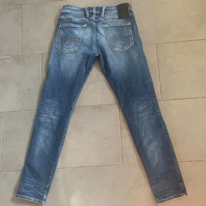 Replay Hyperflex Anbass jeans blå - Säljer ett par Replay Hyperflex Anbass jeans i klassisk blå tvätt med snygga slitningar och kontrastsömmar. Modellen har fem fickor, smal passform och stretchigt material för extra komfort. Perfekta för dig som gillar en modern och stilren look.