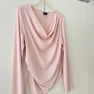 Ljusrosa topp med drapering - Säljer en ljusrosa långärmad topp från gina tricot med snygg draperad front. Toppen har en mjuk, följsam passform och är perfekt för dig som gillar en feminin och trendig stil.