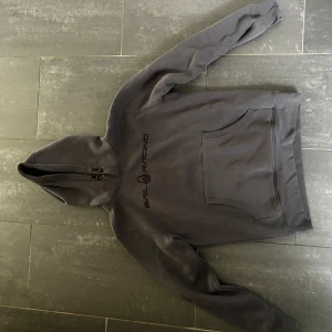 Svart hoodie från Sail Racing - Svart hoodie från Sail Racing med broderad logga på bröstet. Tröjan har huva med snörning och en stor magficka framtill. Mjuk insida och klassisk passform, perfekt för kyliga dagar.