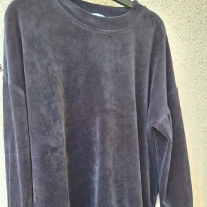 Mörkgrå sammetströja med lång ärm - Mysig och stilren långärmad tröja i mörkgrå sammet. Tröjan har en rund halsringning och en loose passform som ger en avslappnad vibe. Perfekt för dig som gillar mjuka material och enkel design.