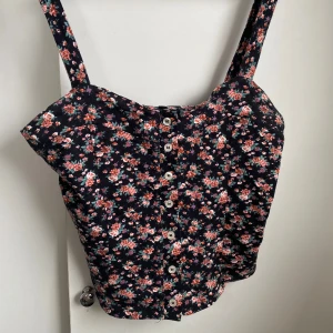 Blommig top  - Supersöt topp från Bik bok. Toppen har breda axelband och knäppning med vita knappar framtill. Perfekt för en somrig look med vintagekänsla.