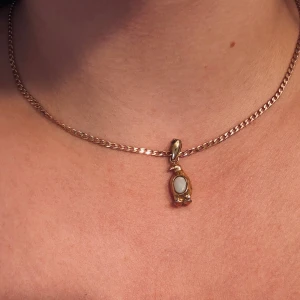Guldigt pingvinberlock till halsband - Unik pingvinberlock i guldton och en vit oval sten på magen. Köpt second hand och har defekter på färgen men annars i bra skick.