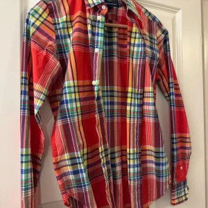 Rutig skjorta från Ralph Lauren Sport - Färgstark rutig skjorta från Ralph Lauren Sport. . Skjortan har långa ärmar, klassisk krage och knäppning framtill. Mönstret är en mix av rött, blått, grönt, gult och lila. Ikoniska broderade loggan på bröstet. Perfekt för dig som gillar färg och preppy stil.