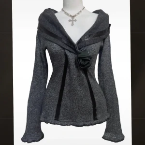 Grå stickad tröja med rosettdetalj - Supersnygg grå stickad tröja med bred krage och svarta satindetaljer längs framsidan. Tröjan har lång ärm, figurnära passform och en stor svart rosett framtil. Tunt stickat!