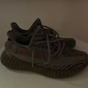 Adidas Yeezy Boost 350 V2 Zebra - Säljer ett par Adidas Yeezy Boost 350 V2 Zebra med grå och svarta zebramönster och diskreta röda detaljer på sidan. Skorna har en stickad ovandel i syntet och en tjock, räfflad sula för extra komfort. Klassisk snörning och rund tå. Perfekta för dig som gillar streetwear.