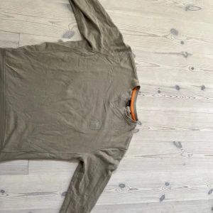 BOSS tröja - Säljer en stilren beige långärmad tröja från BOSS med diskret logga på bröstet. Tröjan har en klassisk passform och är gjord i mjuk bomull. Perfekt för dig som gillar enkel och clean stil.